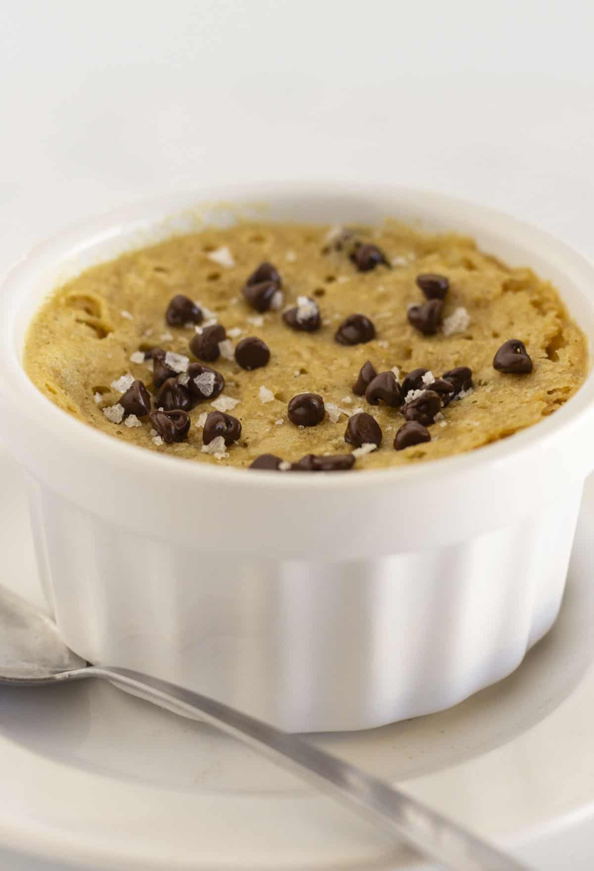 A single serve microwave chocolate chip cookie with flaky sea salt and a spoon.
