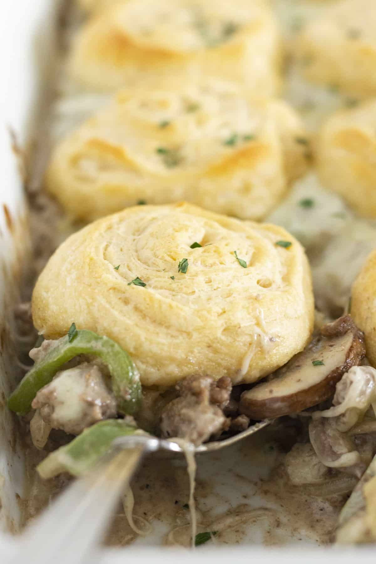 Serving a spoonful of Philly Cheesesteak casserole with crescent roll top.