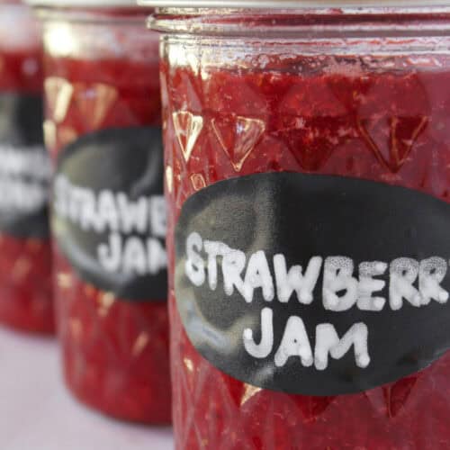 Three jars of strawberry jam with lids and labels.