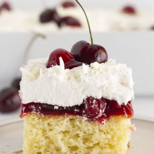 A slice of white forest cake on a white plate with fresh and canned cherries.