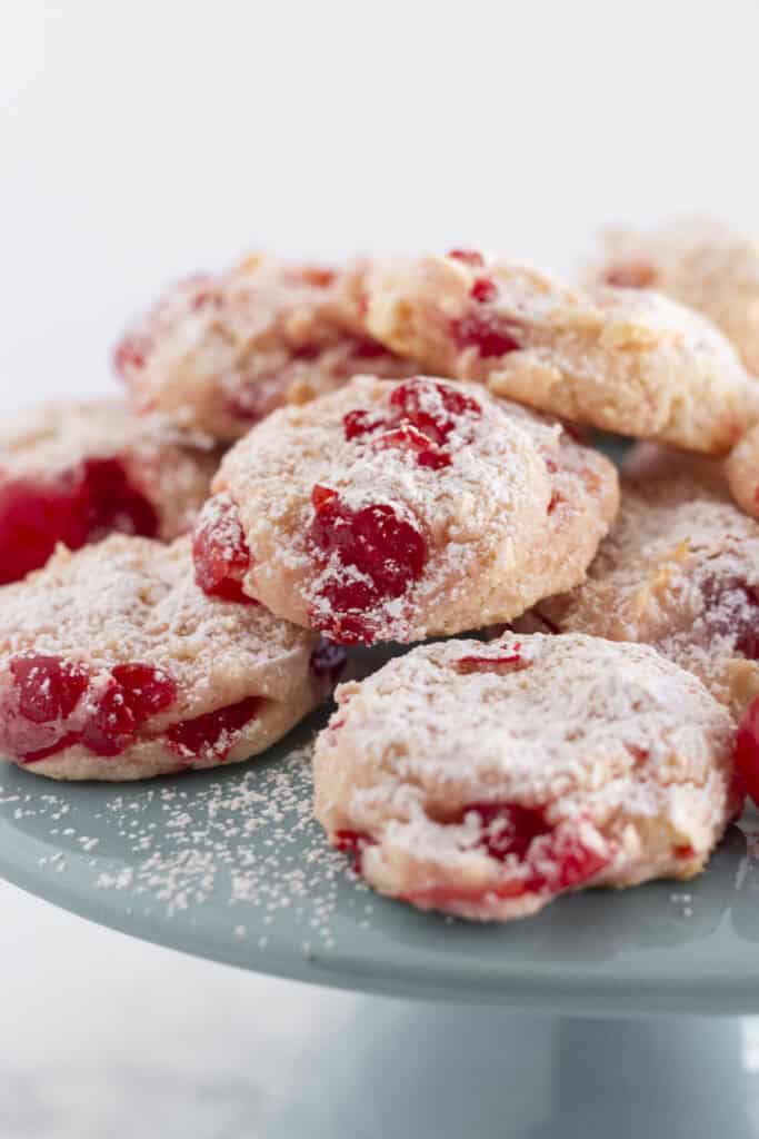Cherry Almond Cookies on a teal cake plate and sprinkled with powdered sugar.
