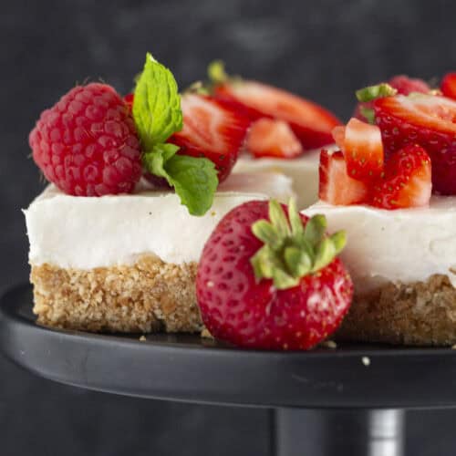 No Bake Cheesecake Bars on a black plate with fresh strawberries.