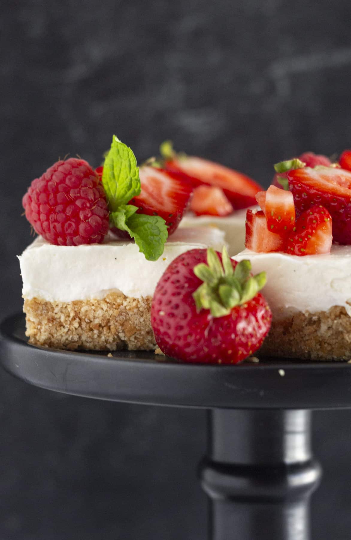 No Bake Cheesecake Bars on a black plate with fresh strawberries.