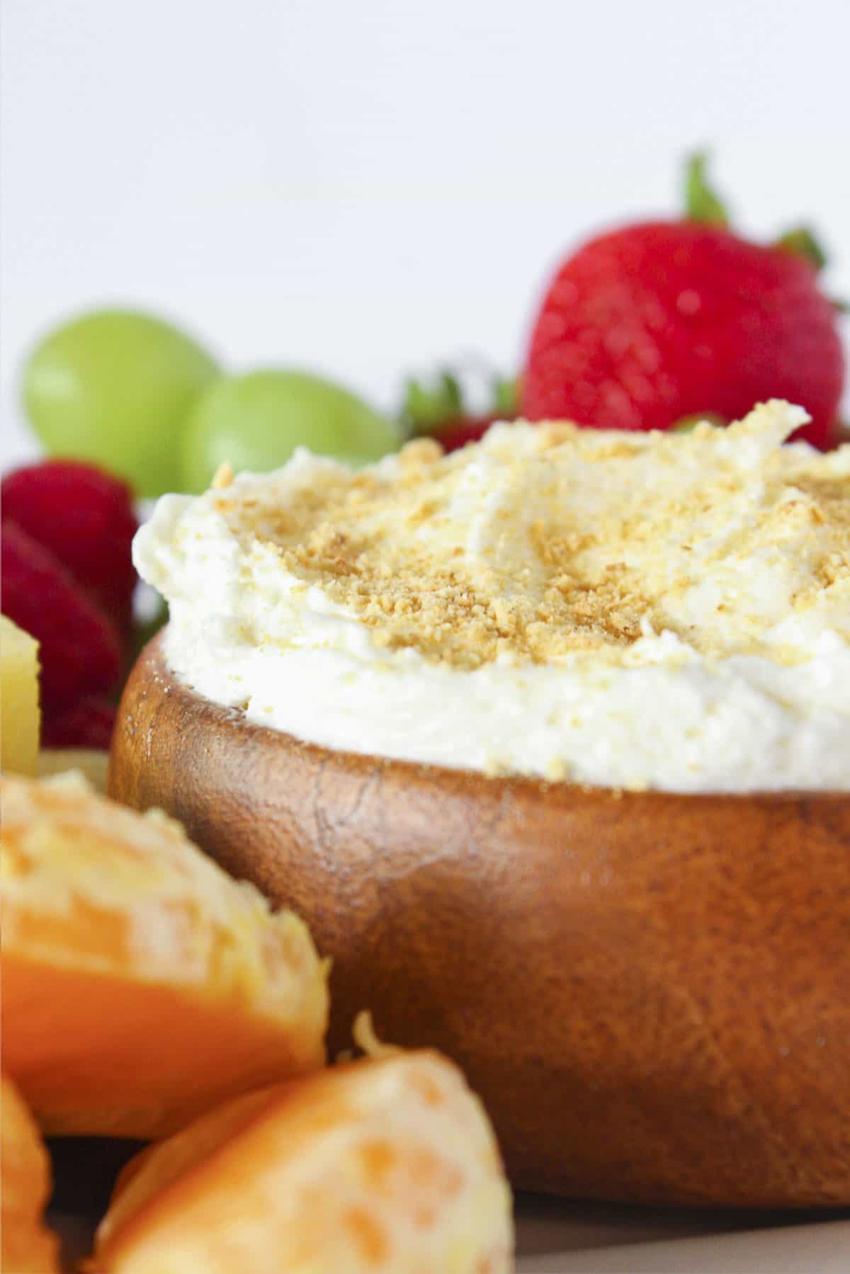 Cheesecake dip for fruit in a wood bowl and served with fresh fruit.