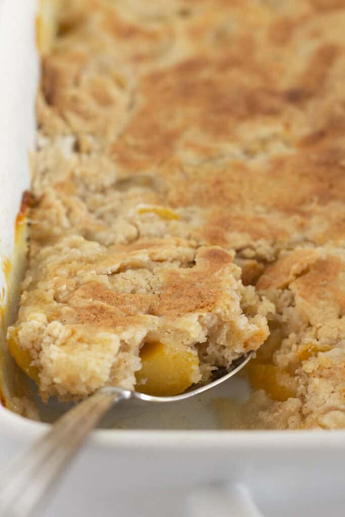 Serving a spoonful of warm peach cake mix cobbler.