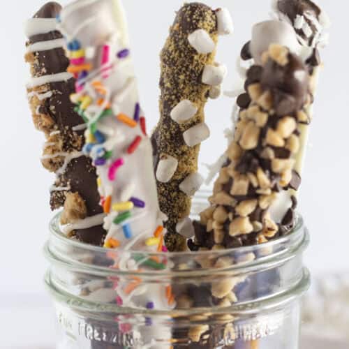 Chocolate covered pretzel rods with toppings, in a mason jar.