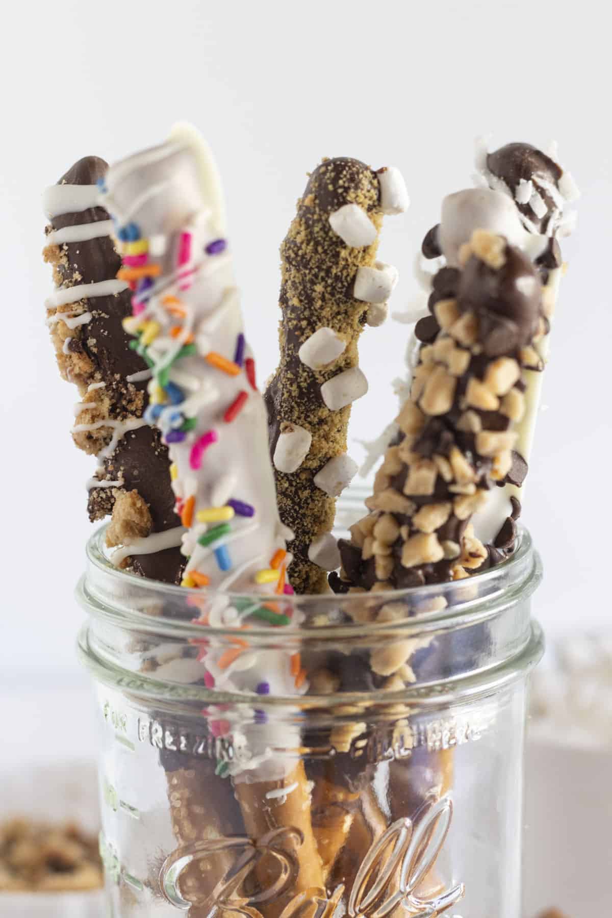 Chocolate covered pretzel rods with toppings, in a mason jar.