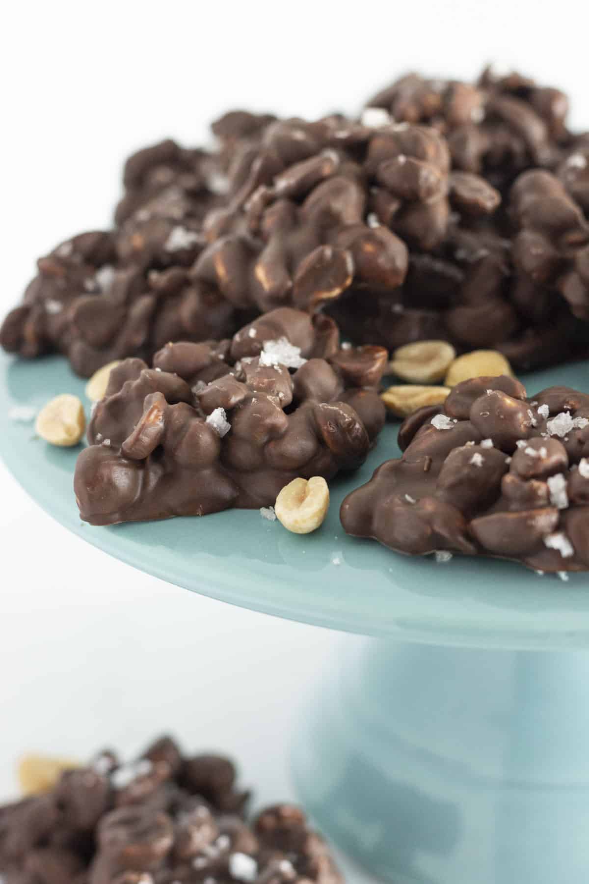 A dozen chocolate covered peanut clusters on a green cake plate.