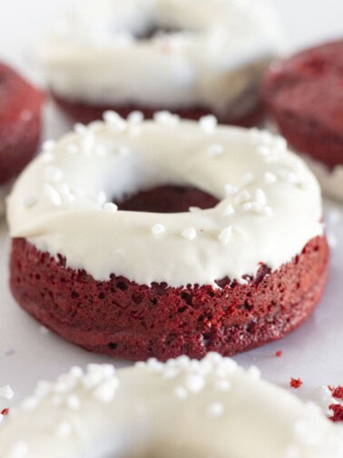 Red velvet cake donut with cream cheese glaze and pearl sugar sprinkles.