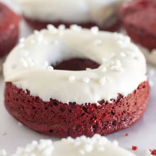 Donut en velours rouge avec glaçage au fromage à la crème et paillettes de sucre perlé.