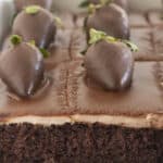 A chocolate covered strawberry cake with a few pieces already eaten.