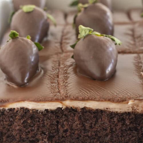 A chocolate covered strawberry cake with a few pieces already eaten.