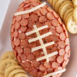 A football pepperoni cheese ball on a white tray with crackers.
