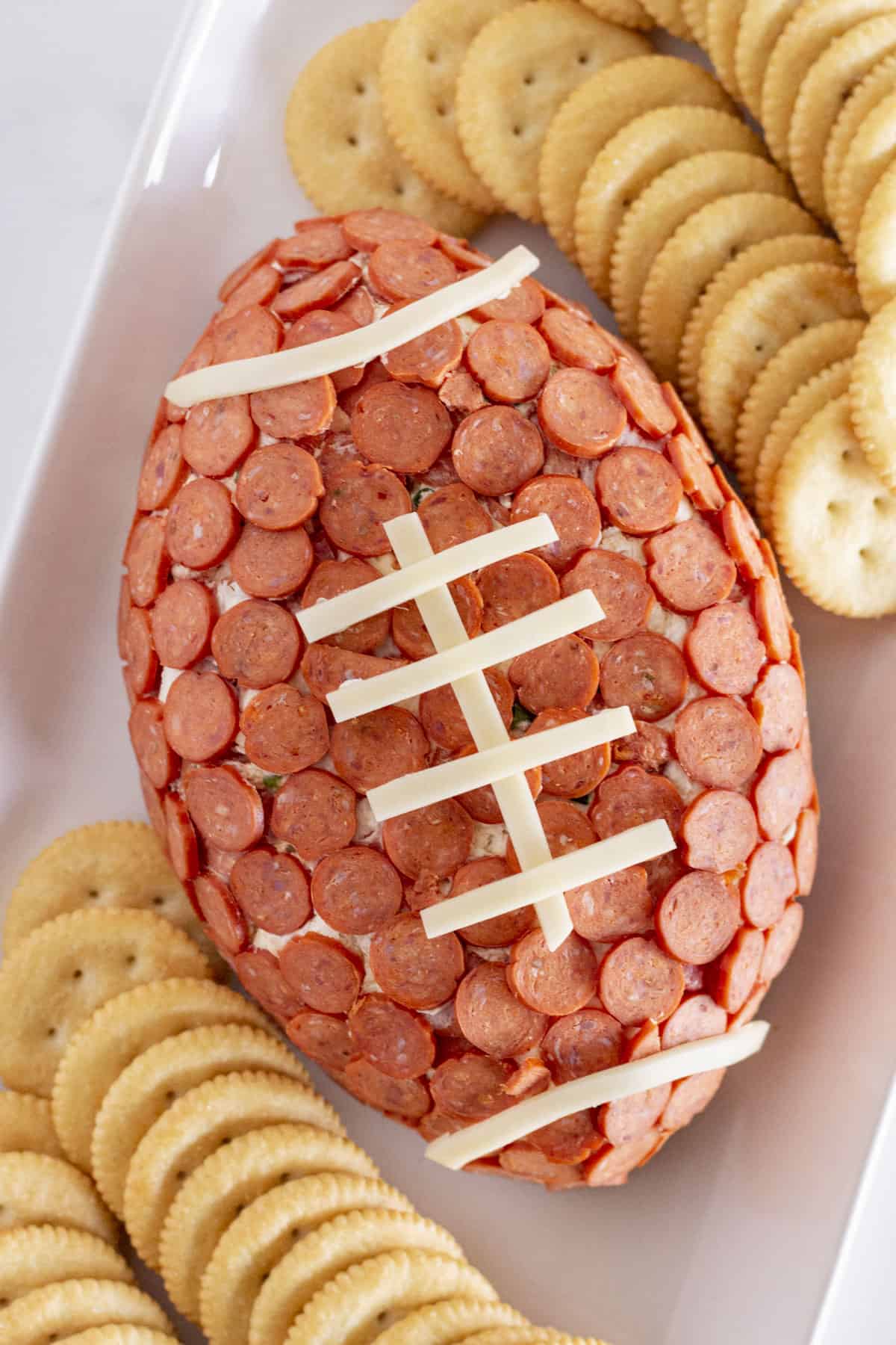 A football pepperoni cheese ball on a white tray with crackers.