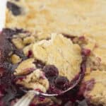 Serving blueberry cobbler with a cake mix from a white pan.
