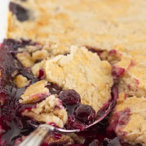 Serving blueberry cobbler with a cake mix from a white pan.