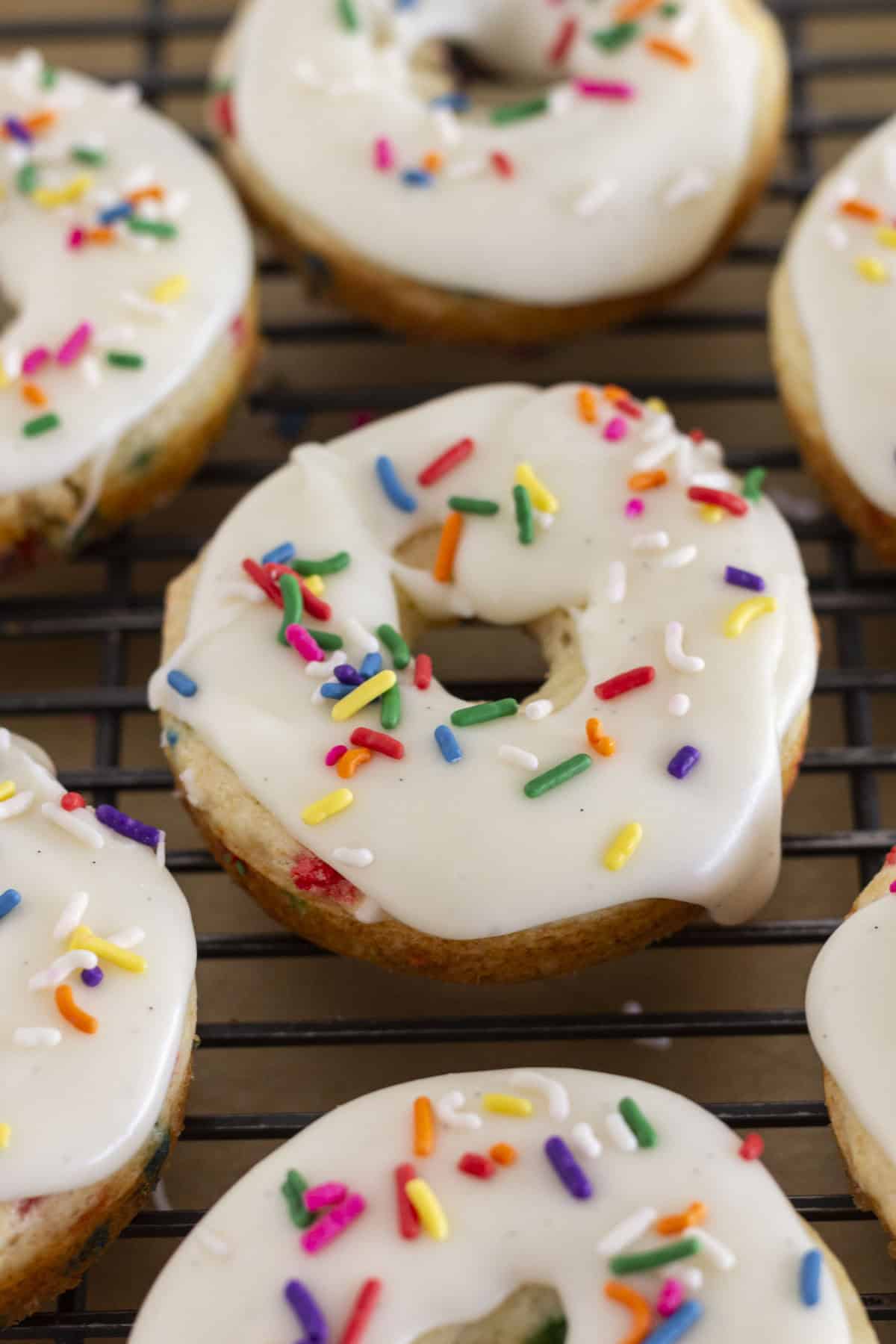 Funfetti donuts on a wire rack with vanilla glaze.