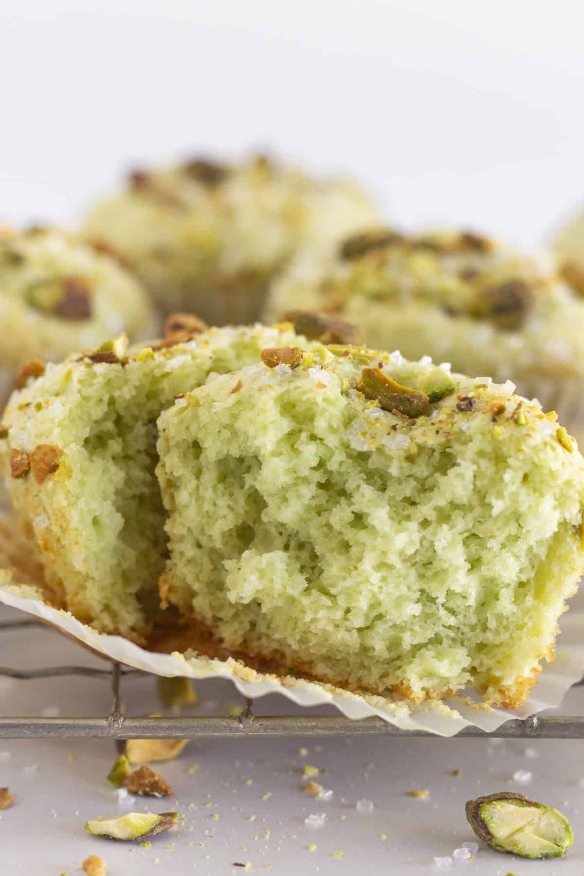 Pistachio muffins on a wire rack with one out of the paper liner and cut in half.