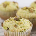 Pistachio muffins on a wire rack with pistachios and sanding sugar on top.