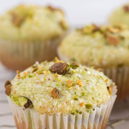Pistachio muffins on a wire rack with pistachios and sanding sugar on top.