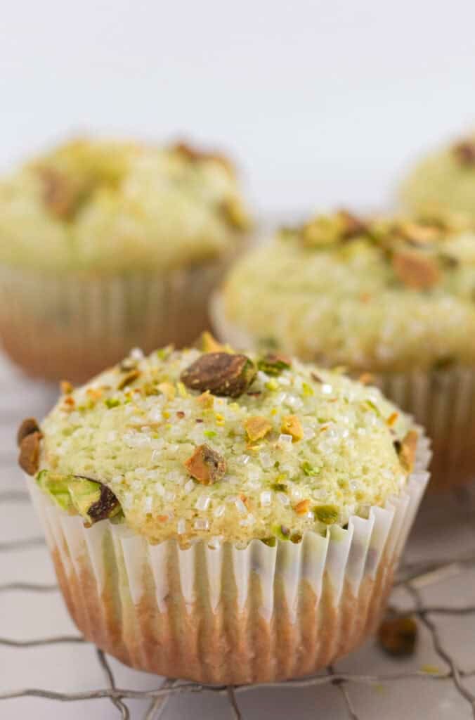 Pistachio muffins on a wire rack with pistachios and sanding sugar on top.