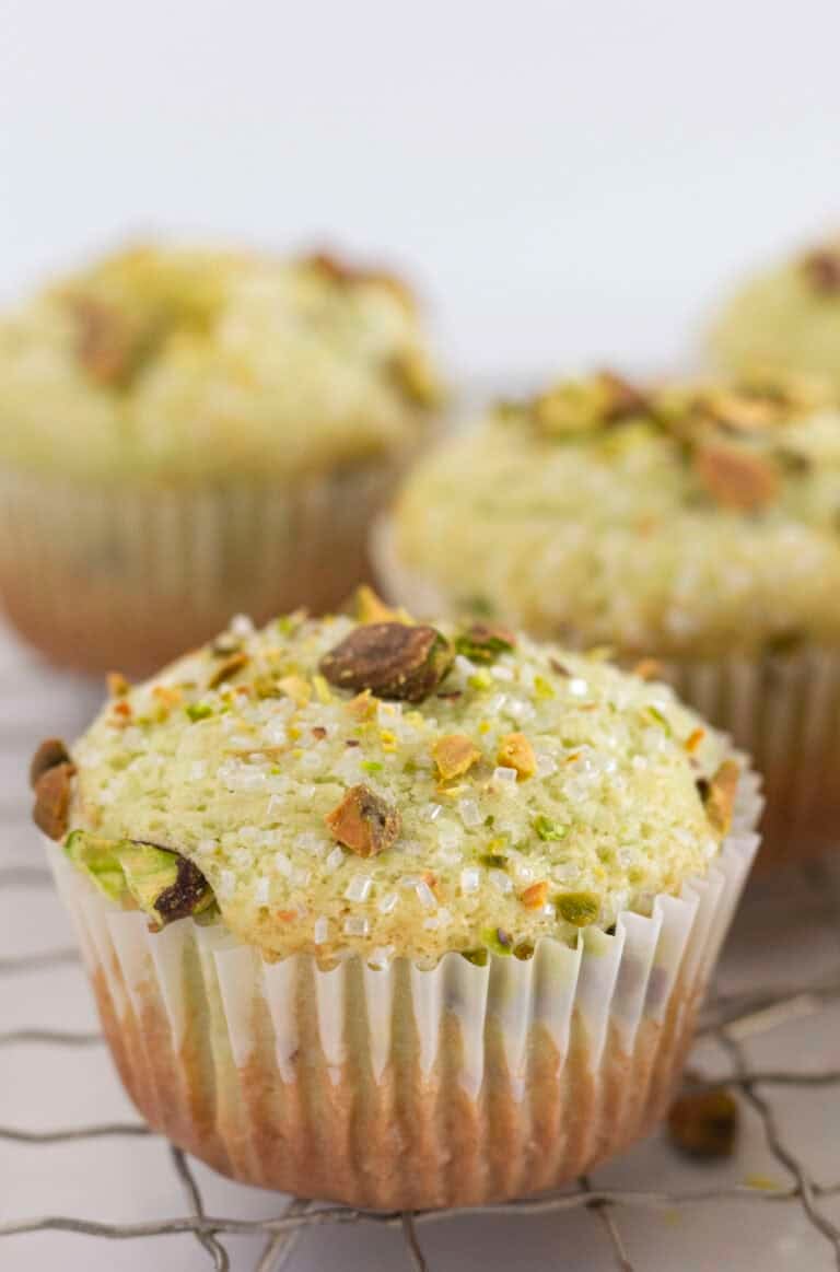 Pistachio muffins on a wire rack with pistachios and sanding sugar on top.