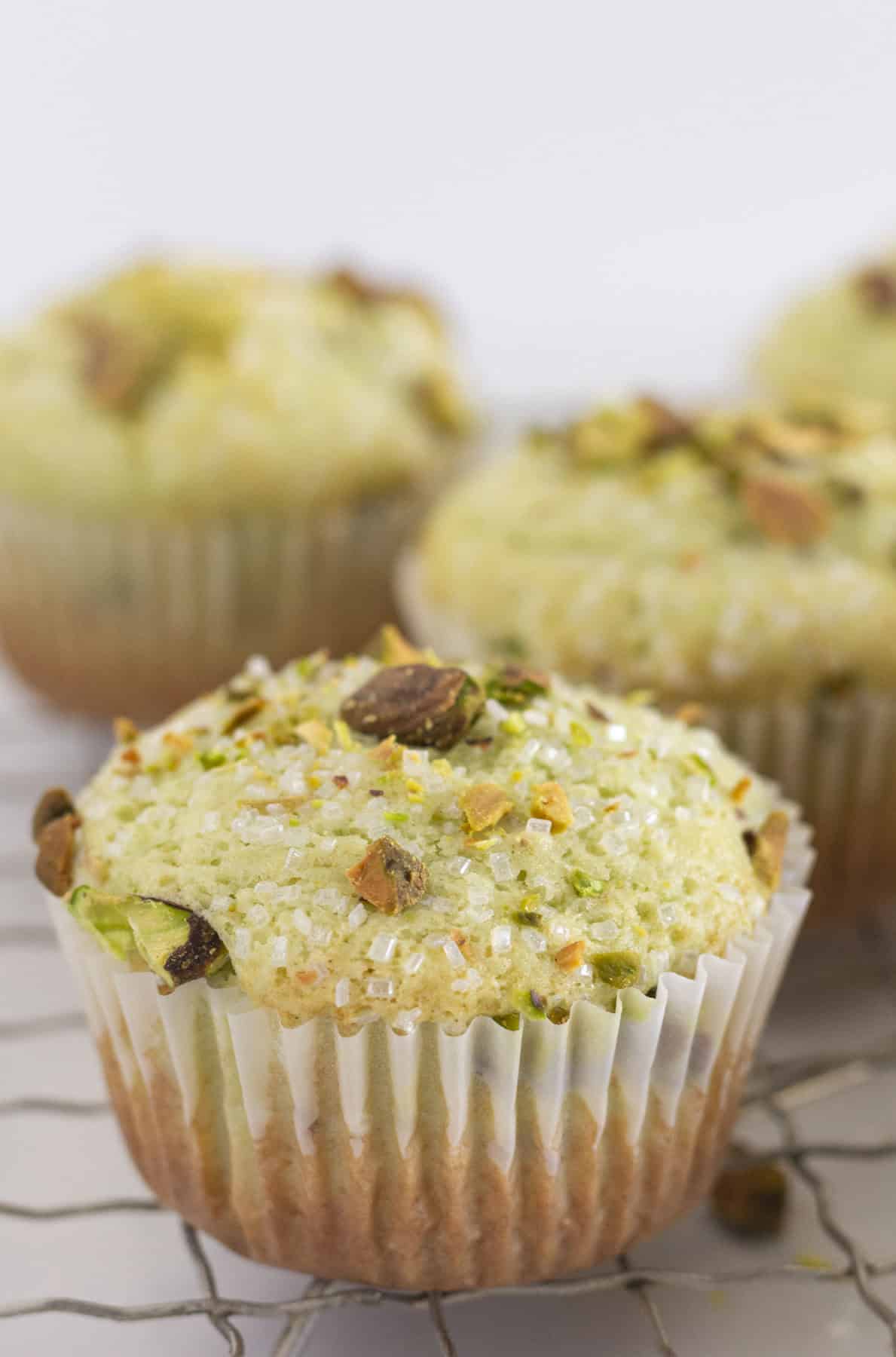 Pistachio muffins on a wire rack with pistachios and sanding sugar on top.