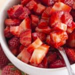 Sugared strawberries in a white bowl with a spoon for serving.