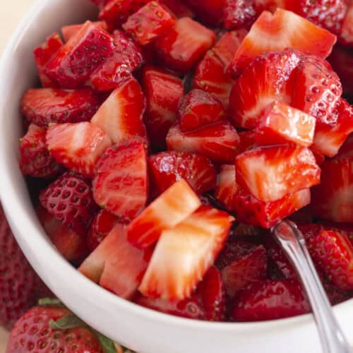 Sugared strawberries in a white bowl with a spoon for serving.