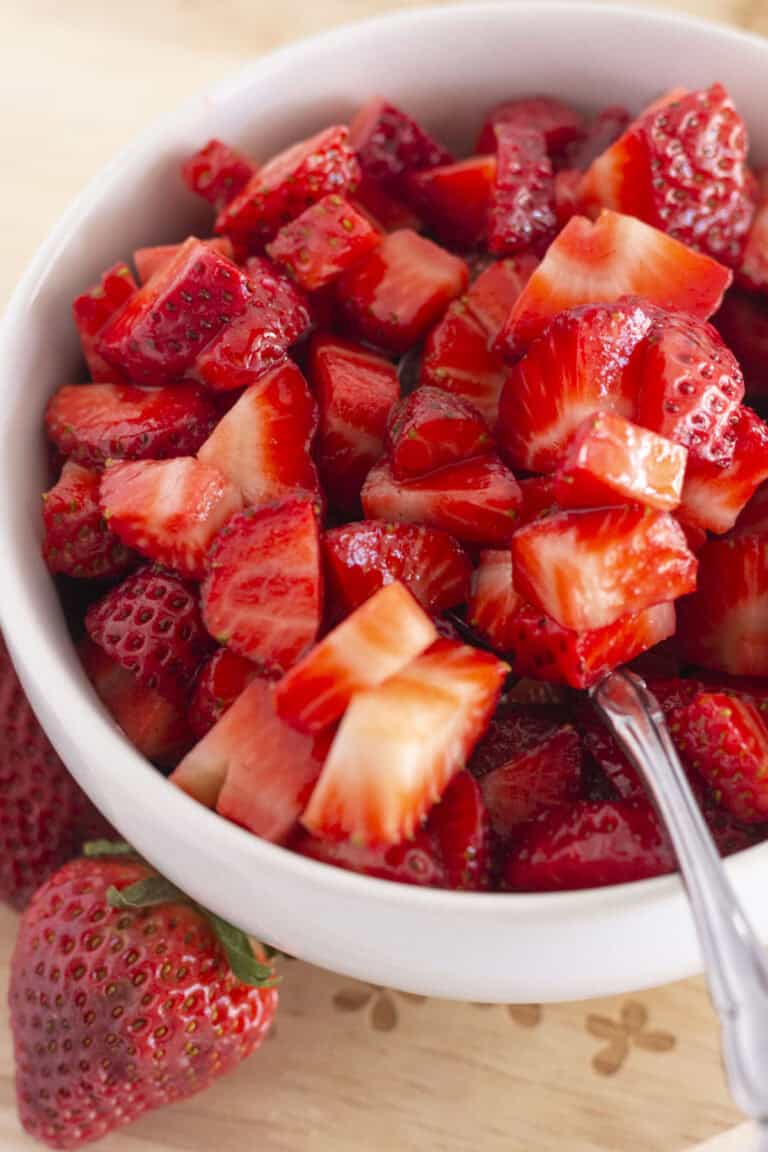 Sugared strawberries in a white bowl with a spoon for serving.