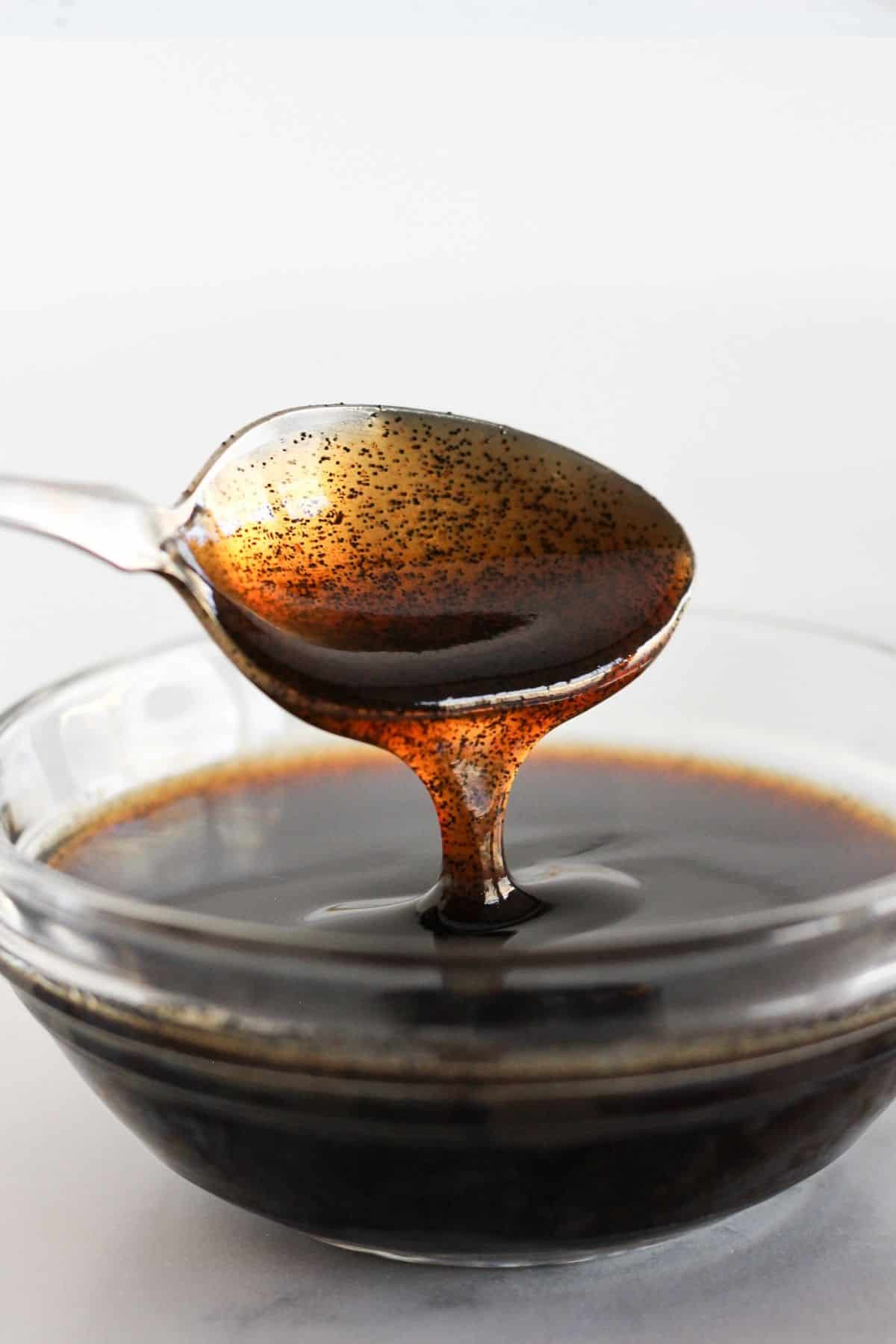 Vanilla bean paste in a clear bowl with a spoon.