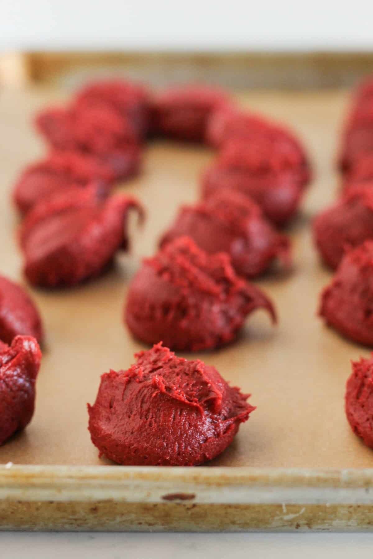 Scoops of red velvet cake mix cookie dough on a baking sheet to chill.