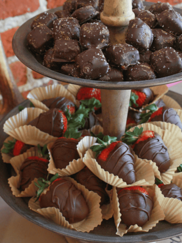 A two tiered stand with chocolate covered strawberries and candy.