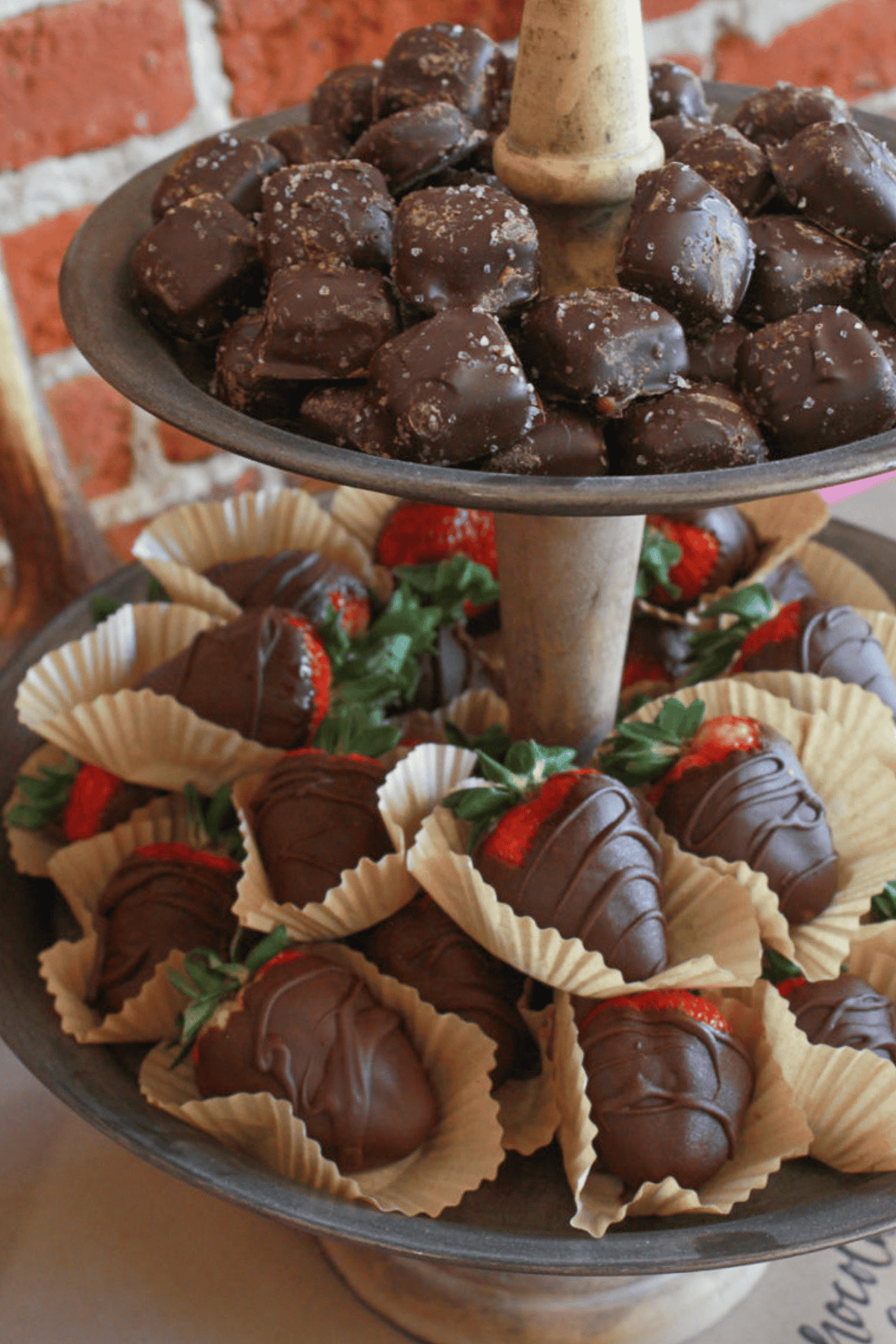 A two tiered stand with chocolate covered strawberries and candy.